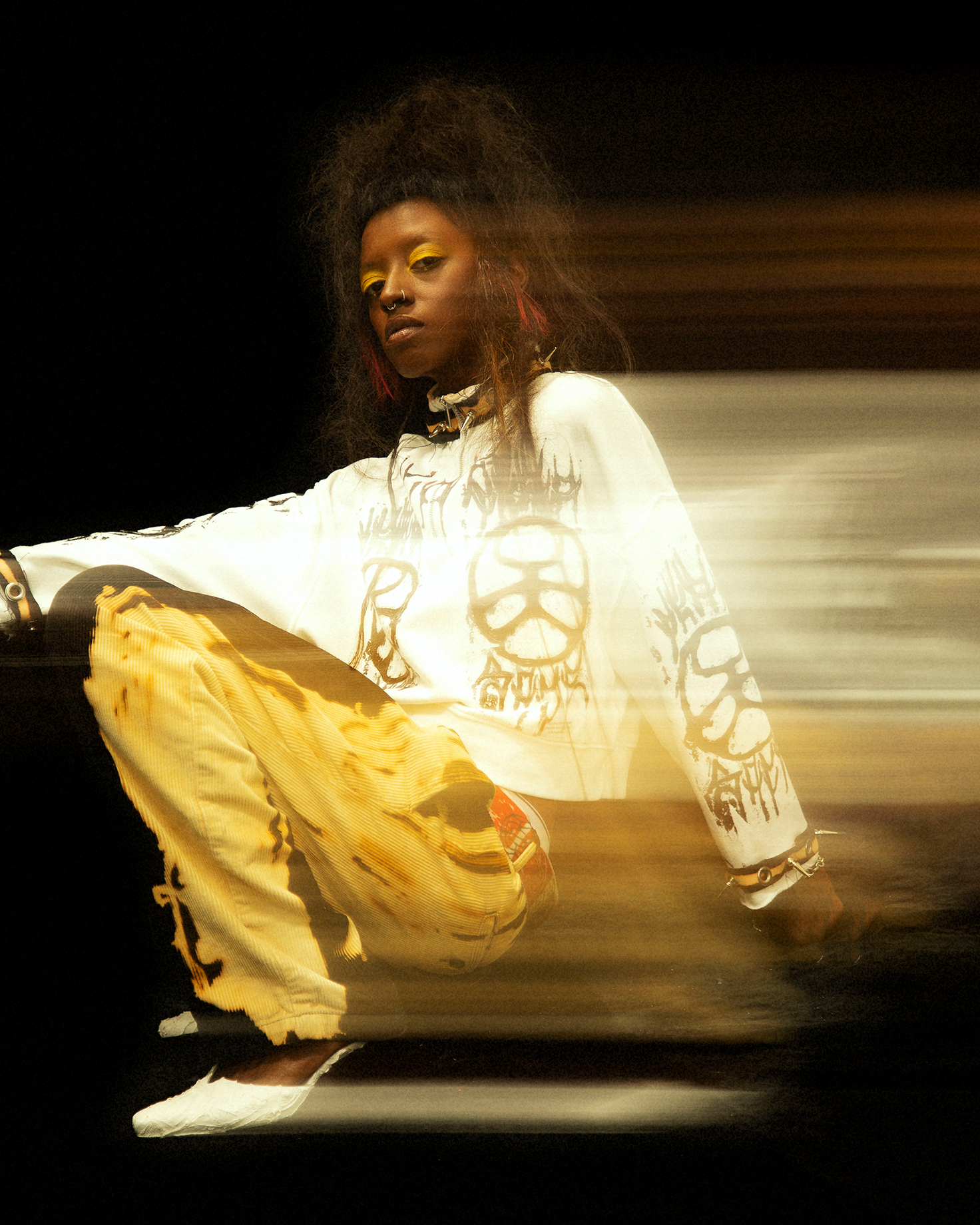 Full body shot of a model crouched with one arm behind them on a black background